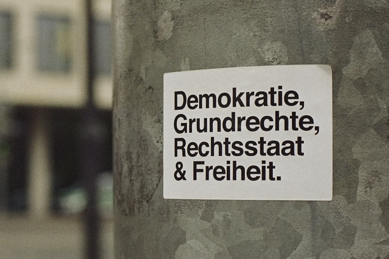 Zettel auf einem Laternenmast in einer Stadt mit der Aufschrift: Demokratie, Grundrechte, Rechtsstaat und Freiheit