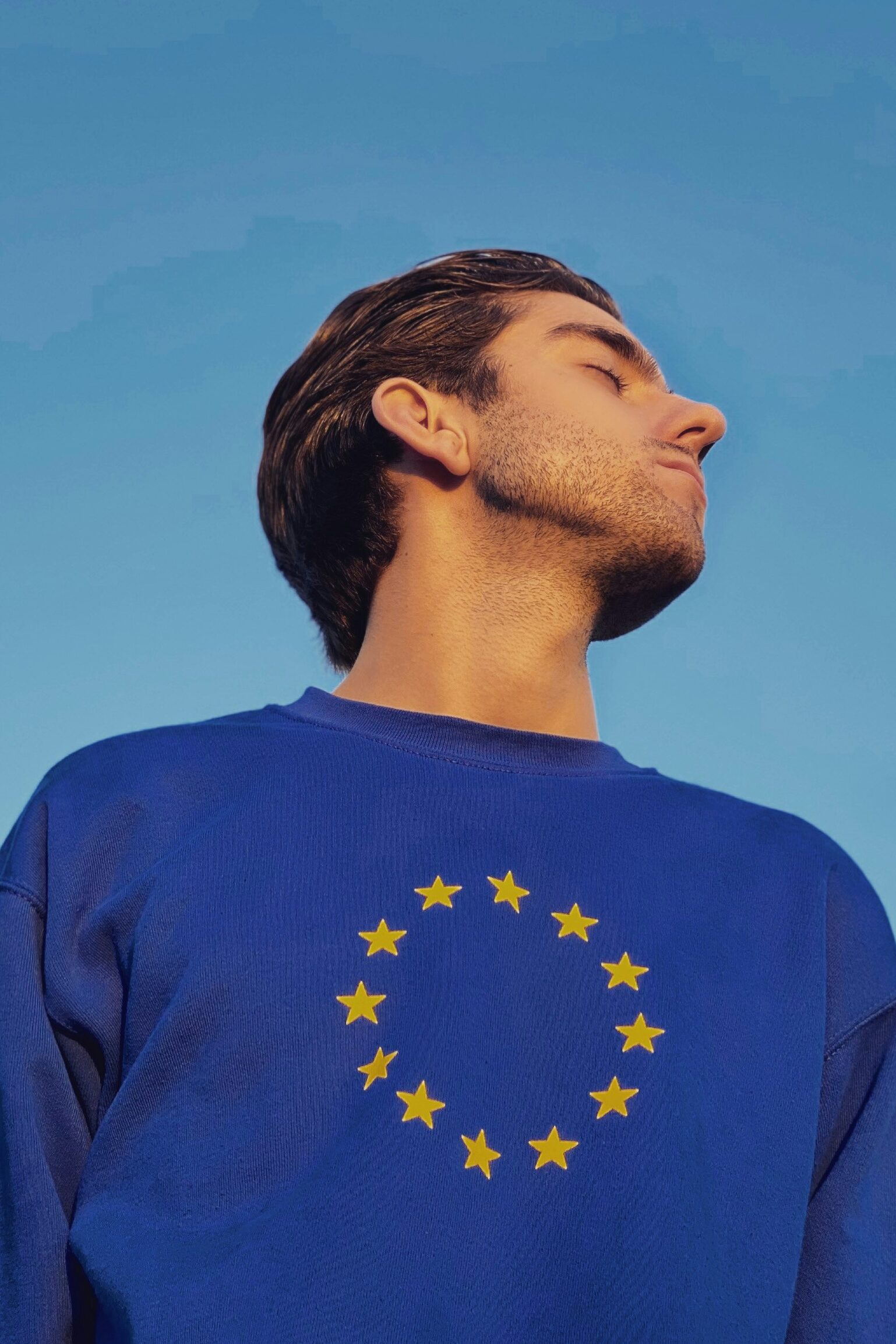 junger Mann mit blauen langärmlichen Shirt, auf dem sich eine Europaflagge befindet.